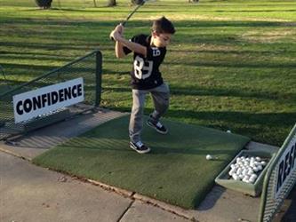 Student at golf driving range swinging golf club