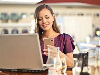 woman with open laptop looking at smartphone