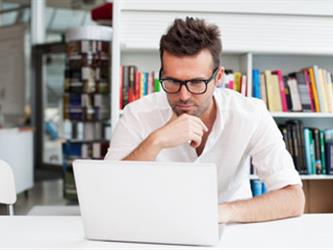 man with glasses looking at open laptop