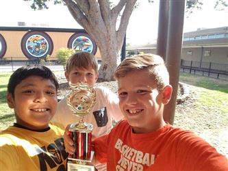 three boys smiling and holding football trophy